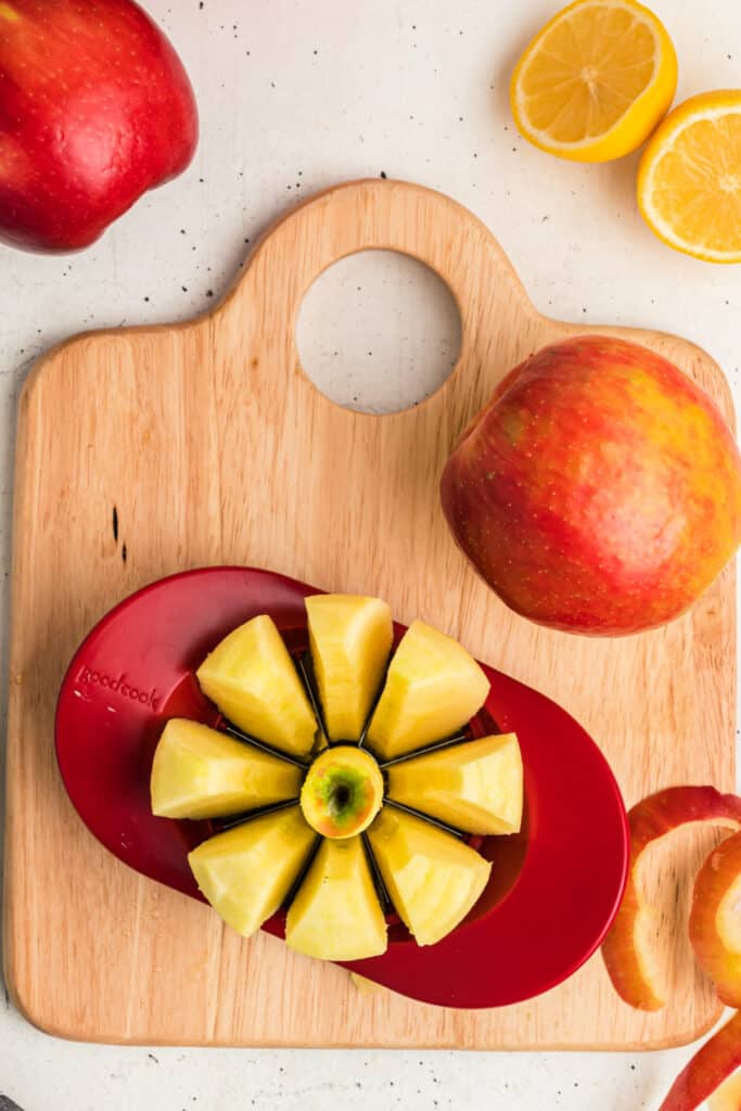 Apple sliced into wedges with a red apple corer on a wooden cutting board.