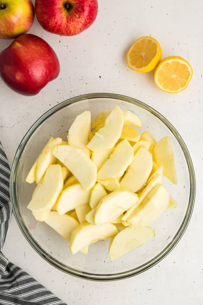 Bowl of freshly sliced apples with halved lemon and whole apples nearby.
