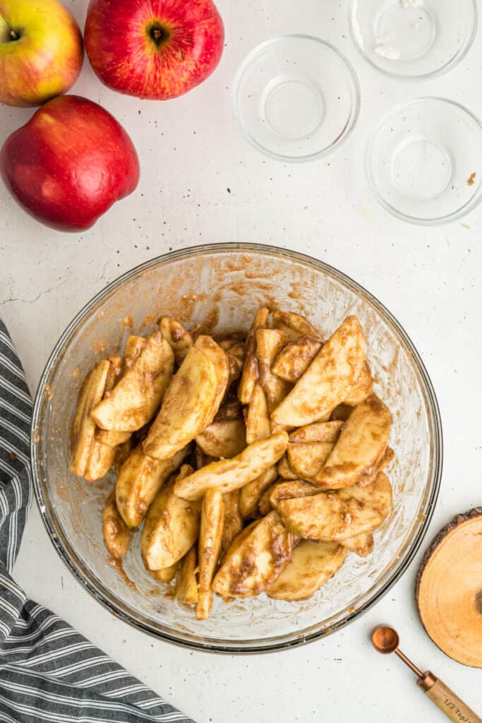 Sliced apples coated in sugar and spices after mixing in a glass bowl.
