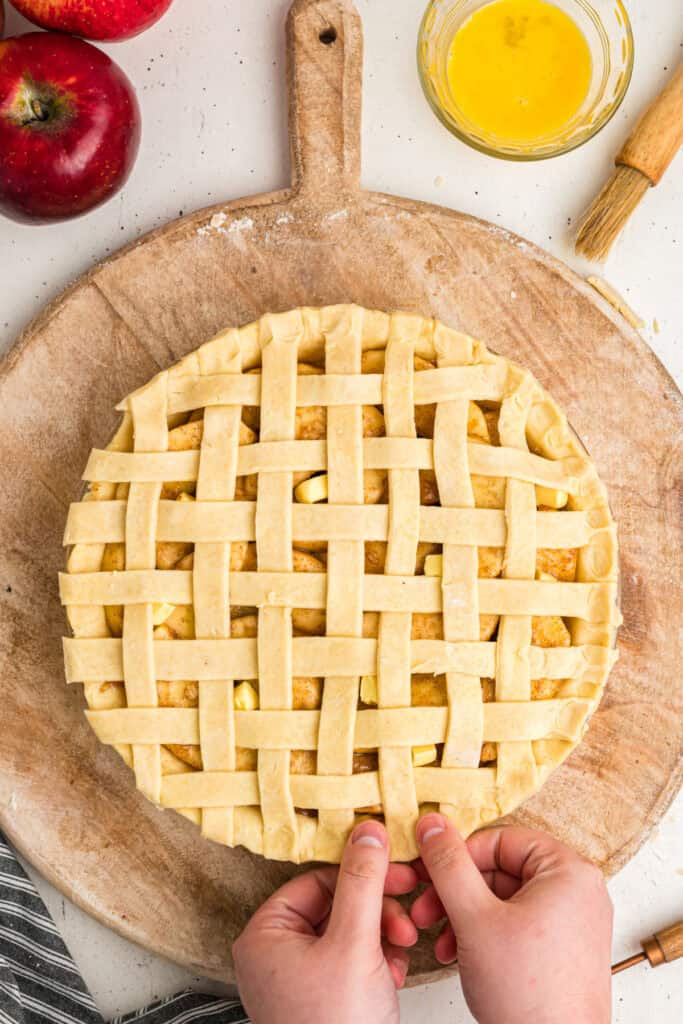 Hands folding trimmed lattice edges under to create clean pie crust border.