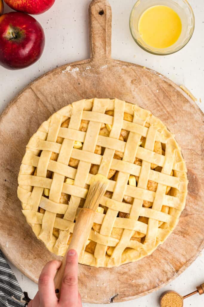 Pastry brush applying egg wash over lattice crust on unbaked apple pie.