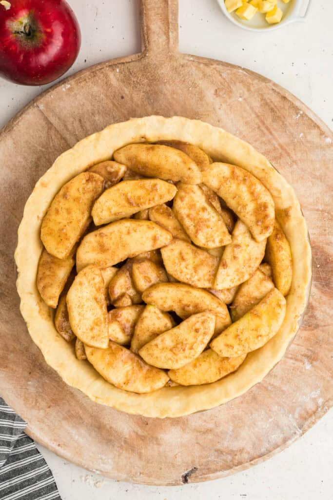 Unbaked pie crust filled with seasoned apple slices on a wooden board.