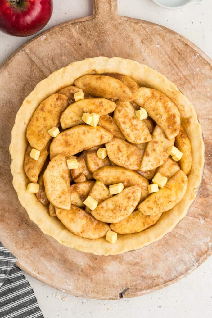 Apple pie filling in crust topped with small cubes of butter before baking.