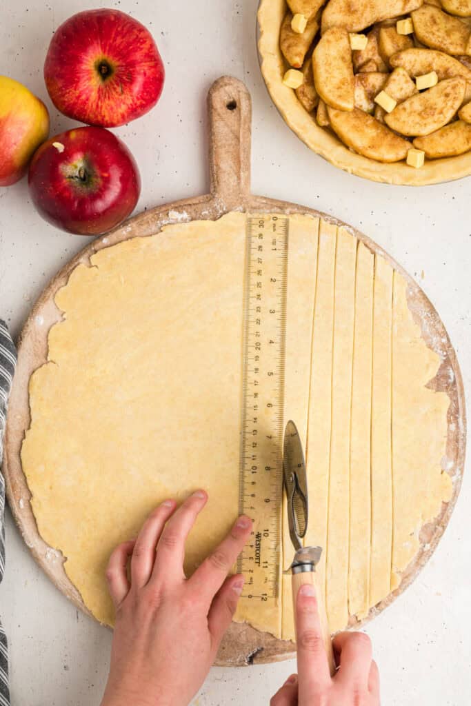 Measuring and cutting strips of pie dough with a ruler and pastry wheel.