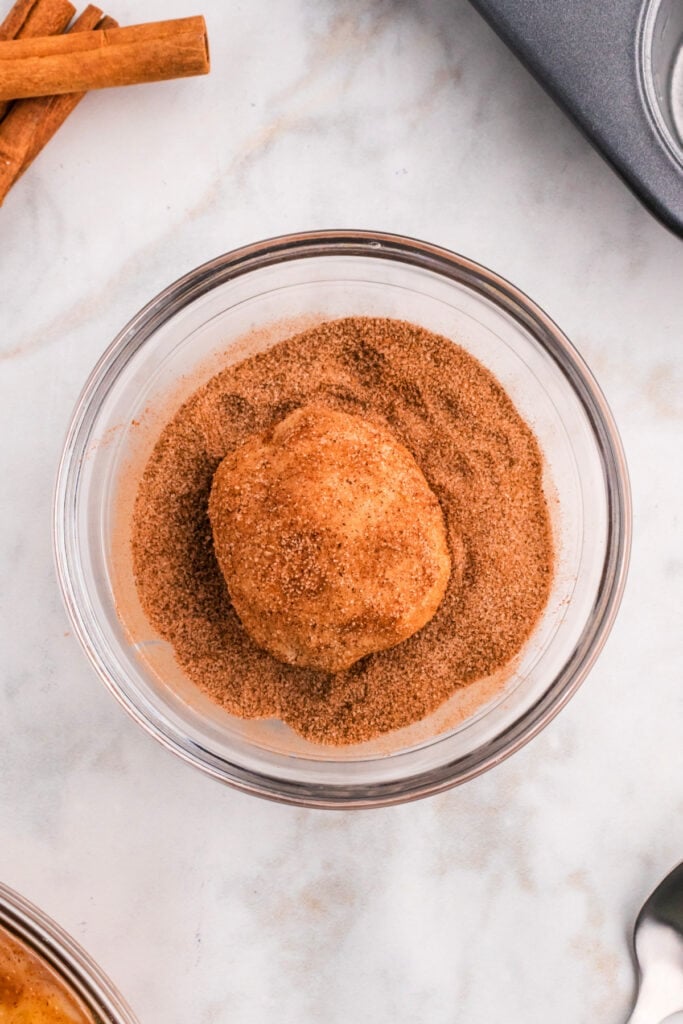 Biscuit dough ball coated in cinnamon sugar mixture for apple pie bombs.
