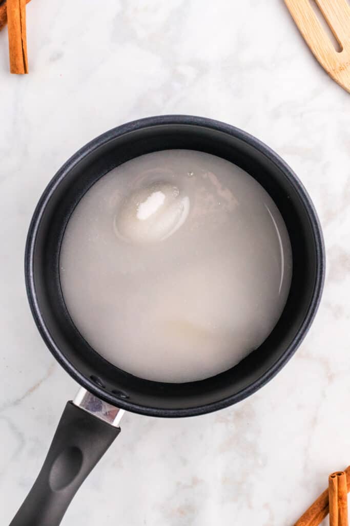 Saucepan with sugar and water mixture beginning to dissolve for spiced caramel sauce.