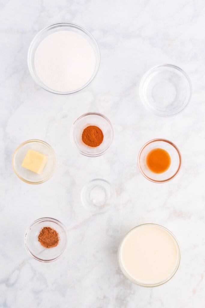 Ingredients for spiced caramel sauce including sugar, cream, butter, vanilla, and spices arranged on a counter.