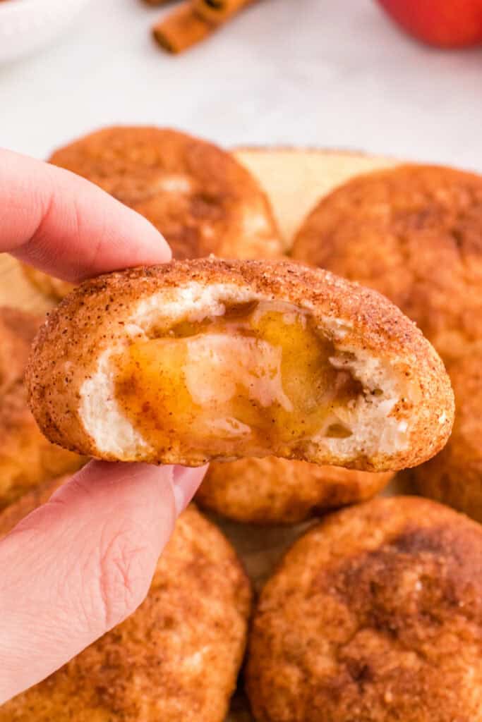 Hand holding an apple pie bomb showing gooey spiced apple filling inside.