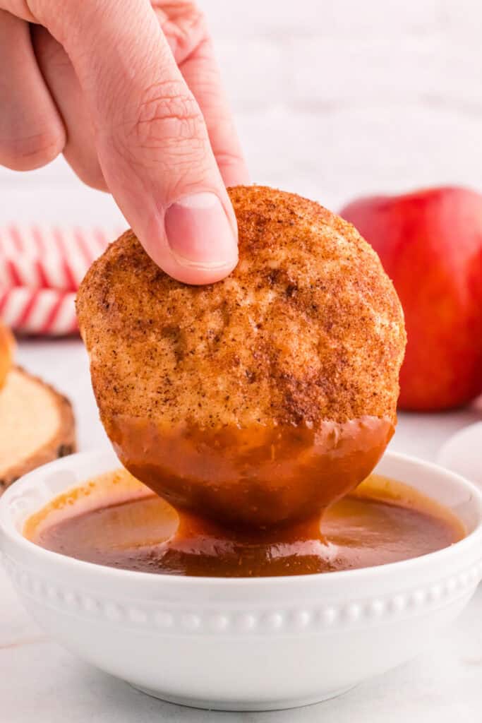 Close-up of an apple pie bomb being dipped into spiced caramel sauce.