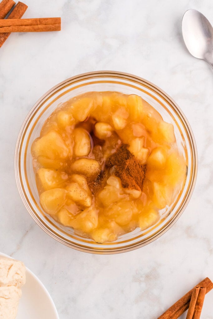 Apple pie filling in a glass bowl with cinnamon and vanilla added for the apple pie bombs recipe.