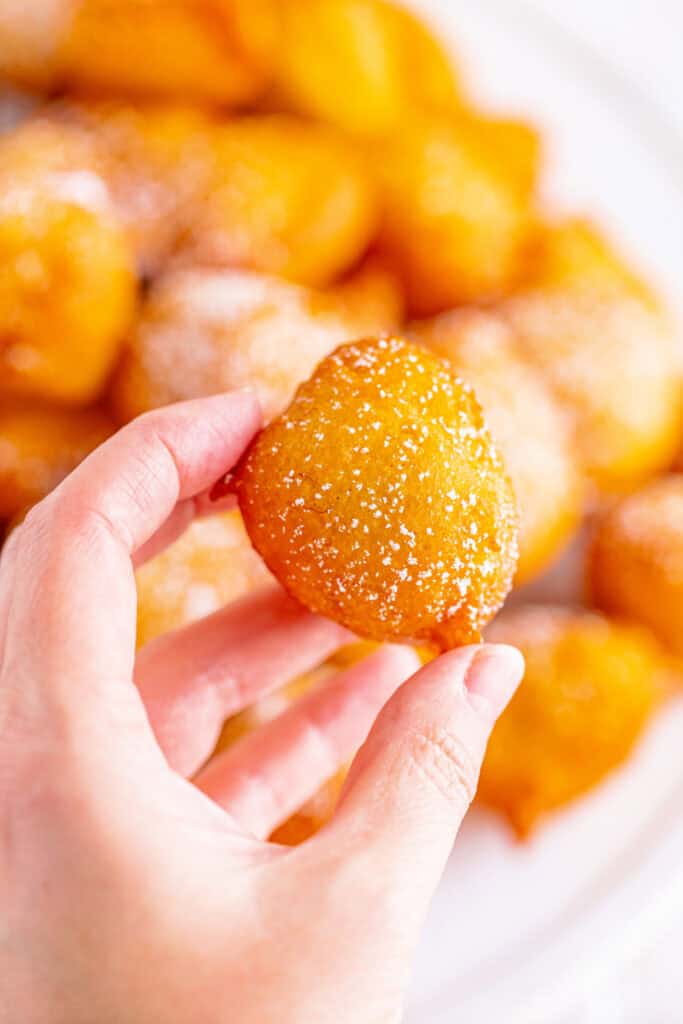 Hand holding a golden banana fritter dusted with powdered sugar, ready to eat