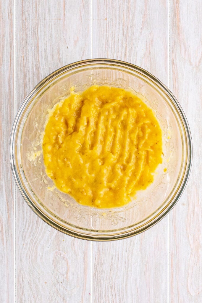 Mashed overripe bananas in a glass mixing bowl ready for banana fritters batter