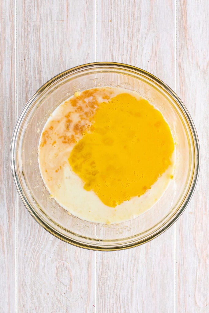 Wet ingredients including mashed bananas, milk, butter, eggs, and vanilla combined in a glass mixing bowl