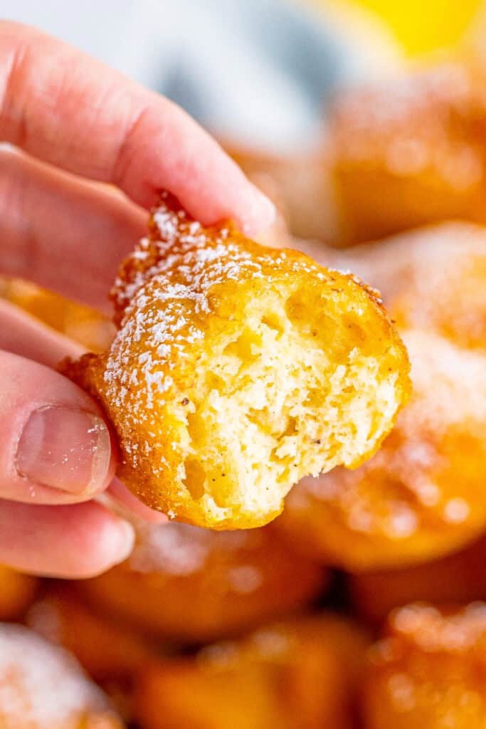 Close-up of a hand holding a banana fritter with a bite taken out, showing soft and fluffy inside texture