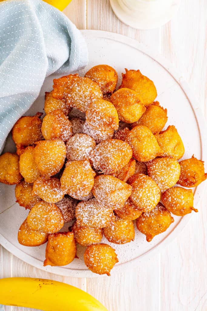 Overhead view of a plate stacked with banana fritters dusted with powdered sugar