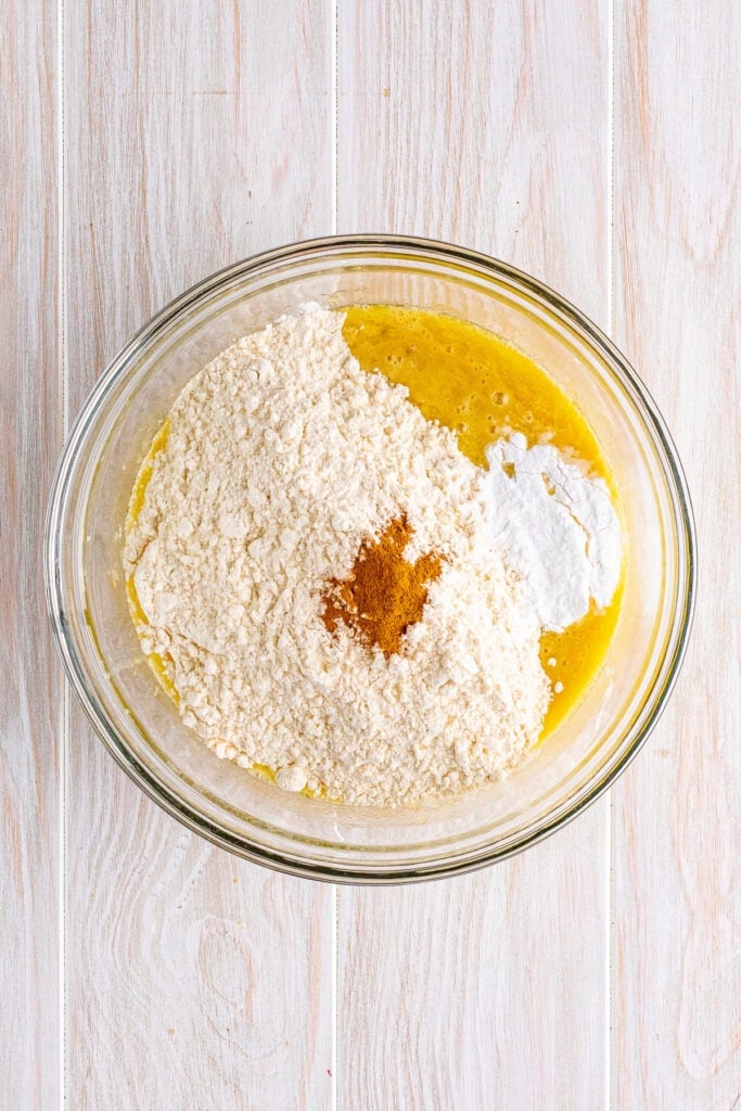 Dry ingredients including flour, baking powder, and cinnamon added to banana mixture in a glass bowl