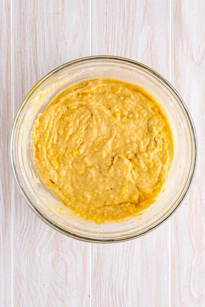 Fully mixed banana fritters batter in a glass mixing bowl, smooth and ready to rest