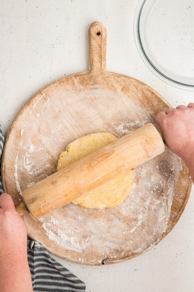Hands rolling out pie crust dough with a wooden rolling pin