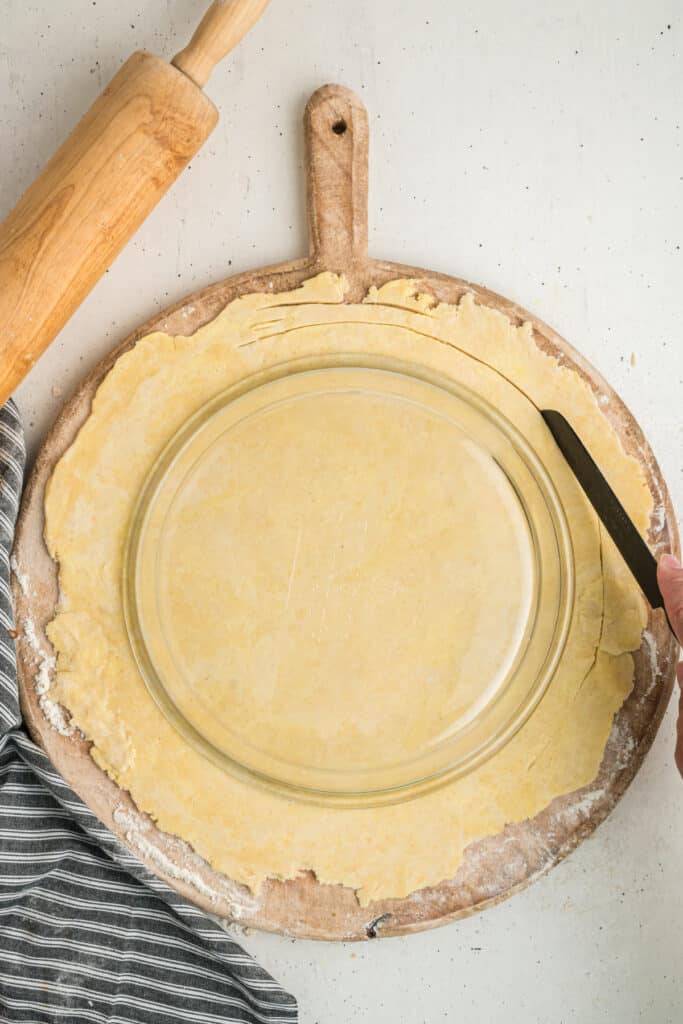 Knife trimming the edges of pie dough using the pie plate as a guide
