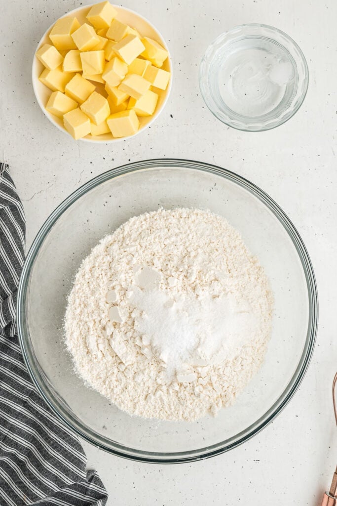 Butter, water, and flour with salt and sugar in a mixing bowl on a light surface