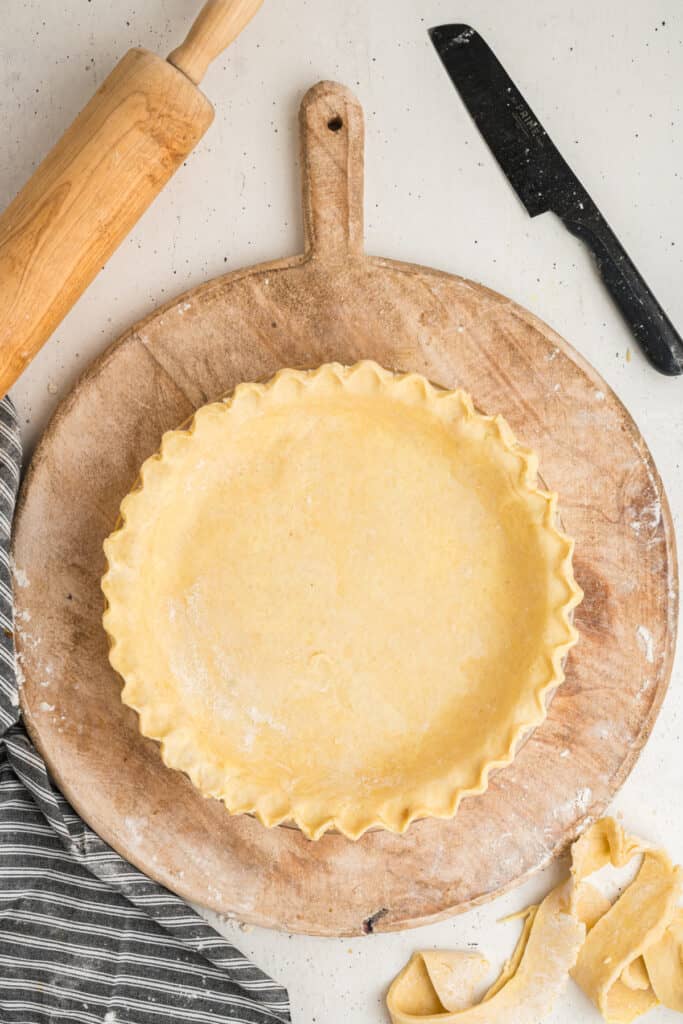 Pie crust with fluted edge formed in a pie dish on a wooden board