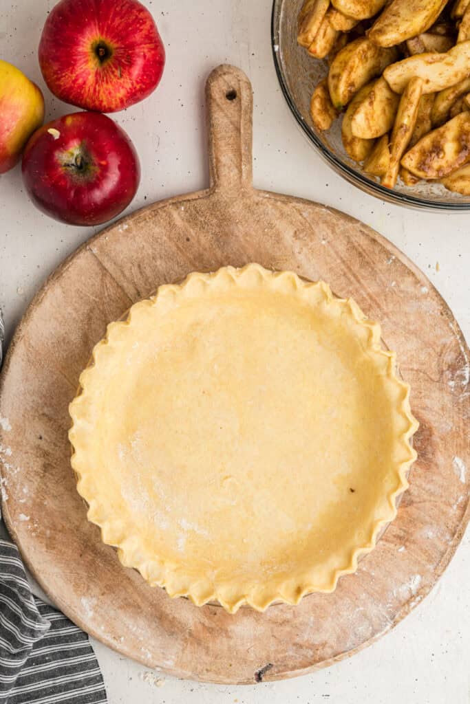Pie crust ready for filling, surrounded by apples and spiced apple slices