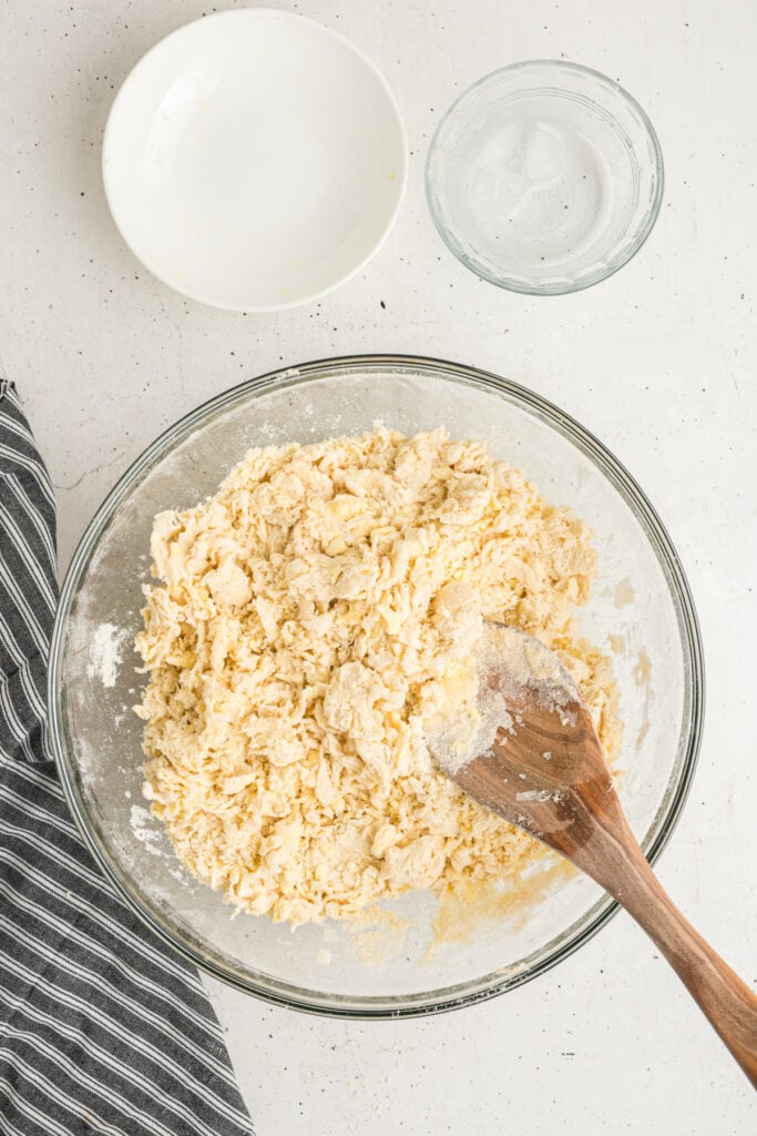 Wooden spoon mixing pie crust dough after adding water