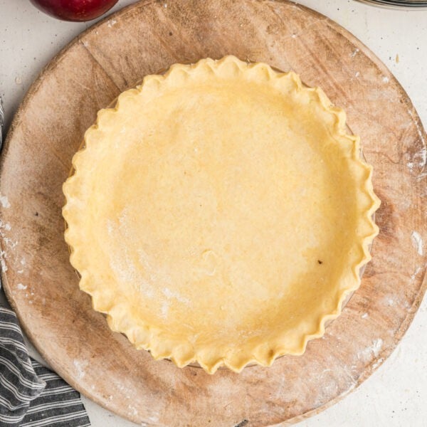 Square image of crimped butter pie crust in a glass pie dish, ready to bake