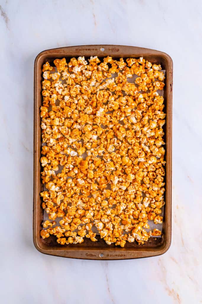 Baking sheet lined with parchment paper and evenly spread baked caramel corn