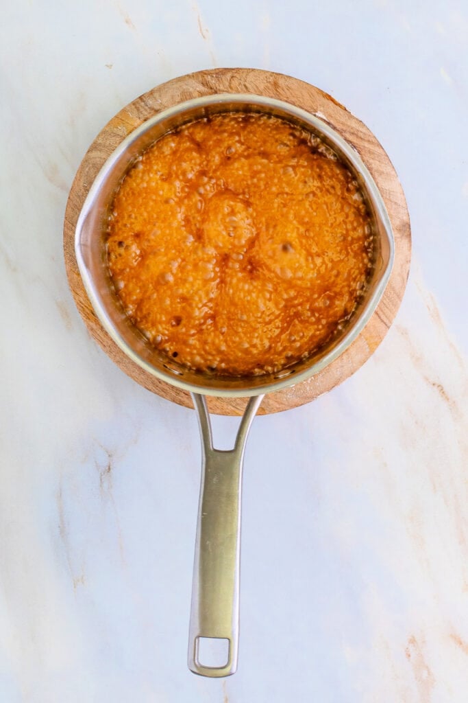 Saucepan with bubbling golden caramel mixture on a wooden trivet