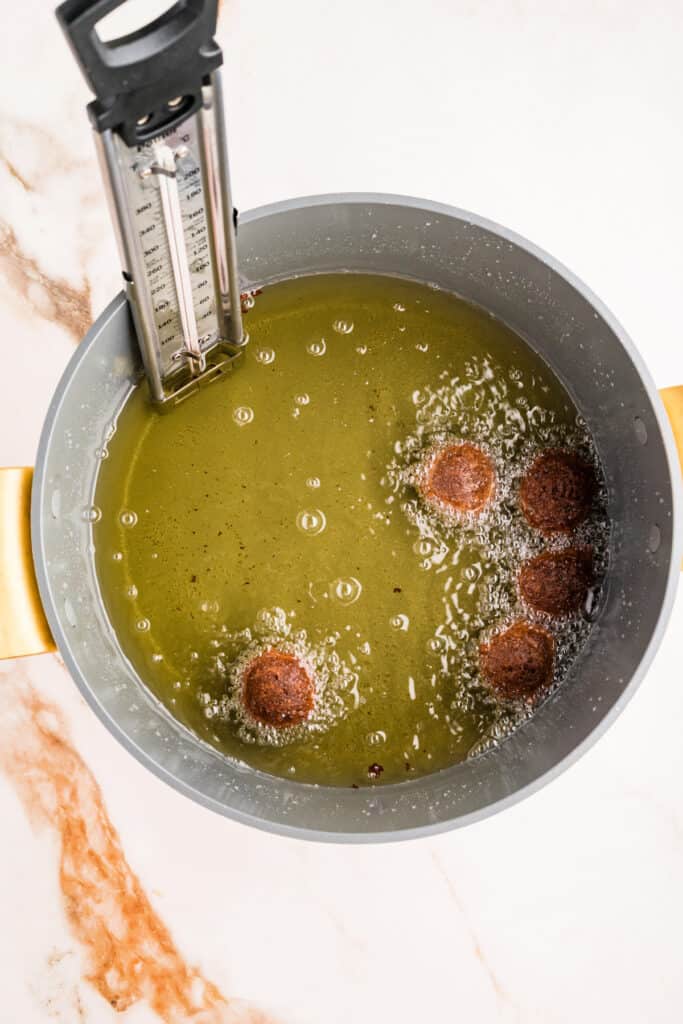 Chocolate donut holes frying in hot oil with thermometer visible