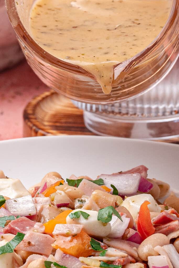 Close-up of vinaigrette being poured over grinder dense bean salad in a serving bowl.