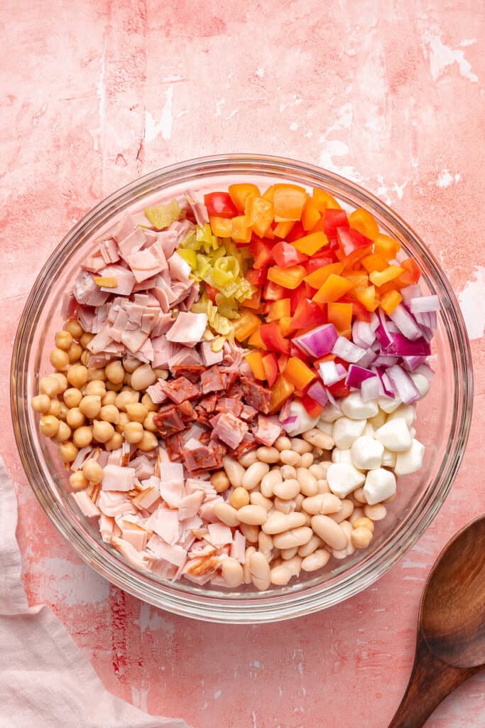 Glass mixing bowl filled with salad ingredients arranged in sections before mixing.
