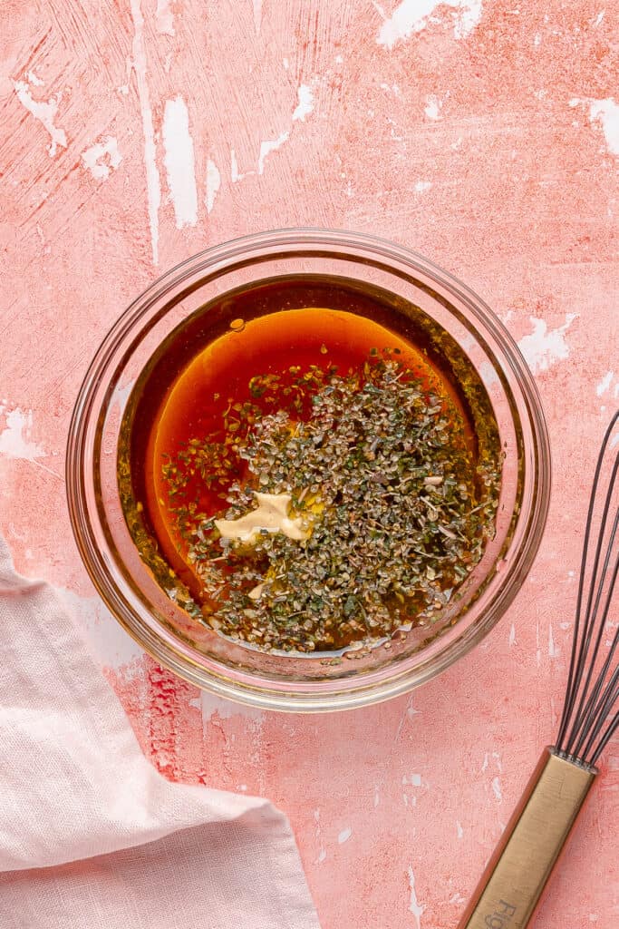 Small glass bowl with vinaigrette ingredients including oil, vinegar, mustard, garlic, and Italian seasoning before whisking.