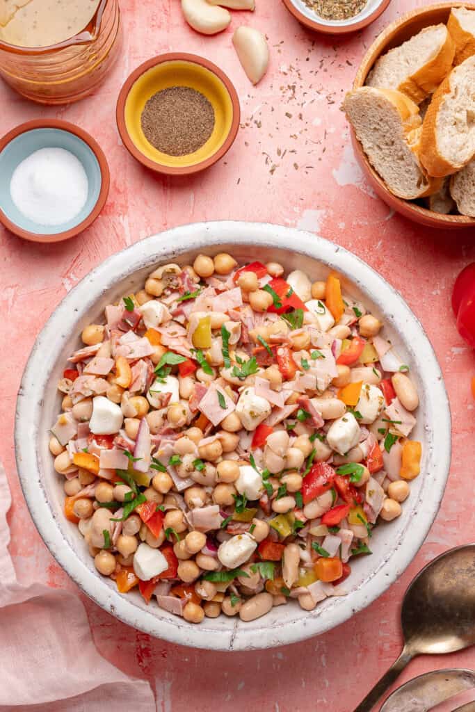 Overhead view of grinder dense bean salad in a white serving bowl, garnished with fresh parsley.
