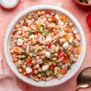 Overhead shot of grinder dense bean salad in a white serving bowl, garnished with fresh parsley.