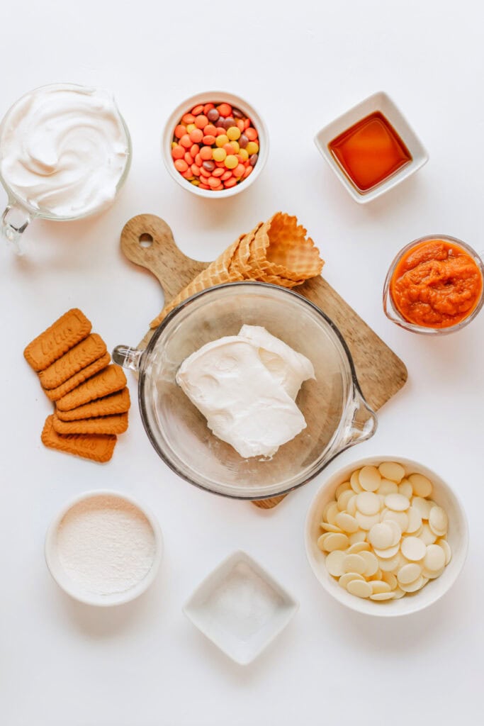 Overhead shot of all ingredients laid out including cream cheese, candy melts, pumpkin mix, and waffle cones