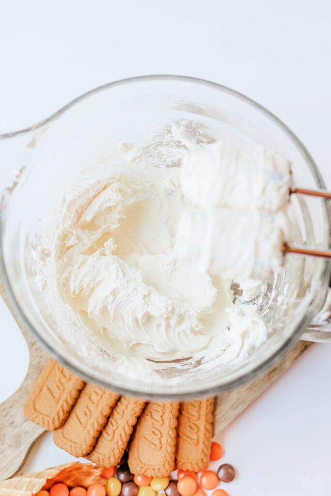 Cream cheese whipped until smooth in a glass bowl with mixer attachments visible