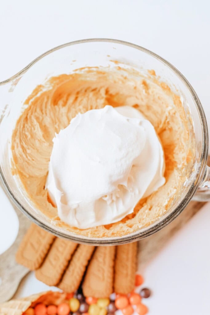 Cool Whip added to the pumpkin cheesecake mixture in a glass bowl
