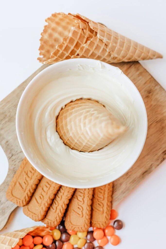 Waffle cone dipped into melted white chocolate in a white bowl