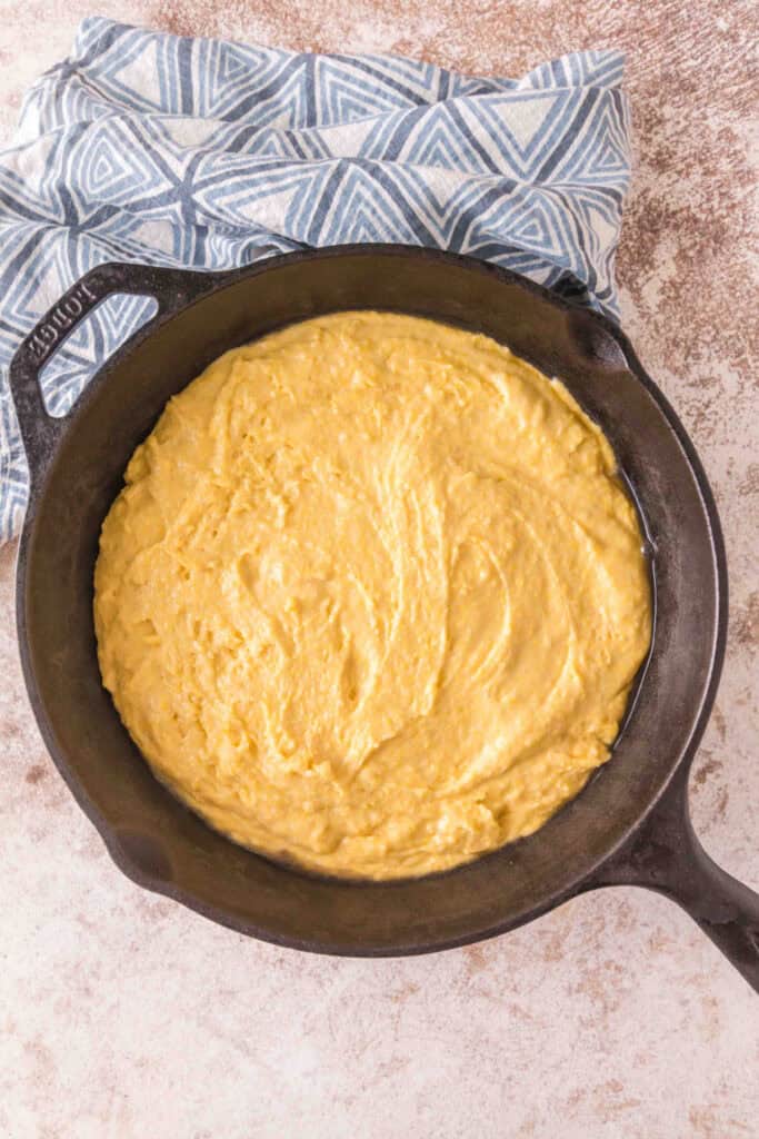 Raw cornbread batter spread evenly in a hot cast iron skillet before baking.