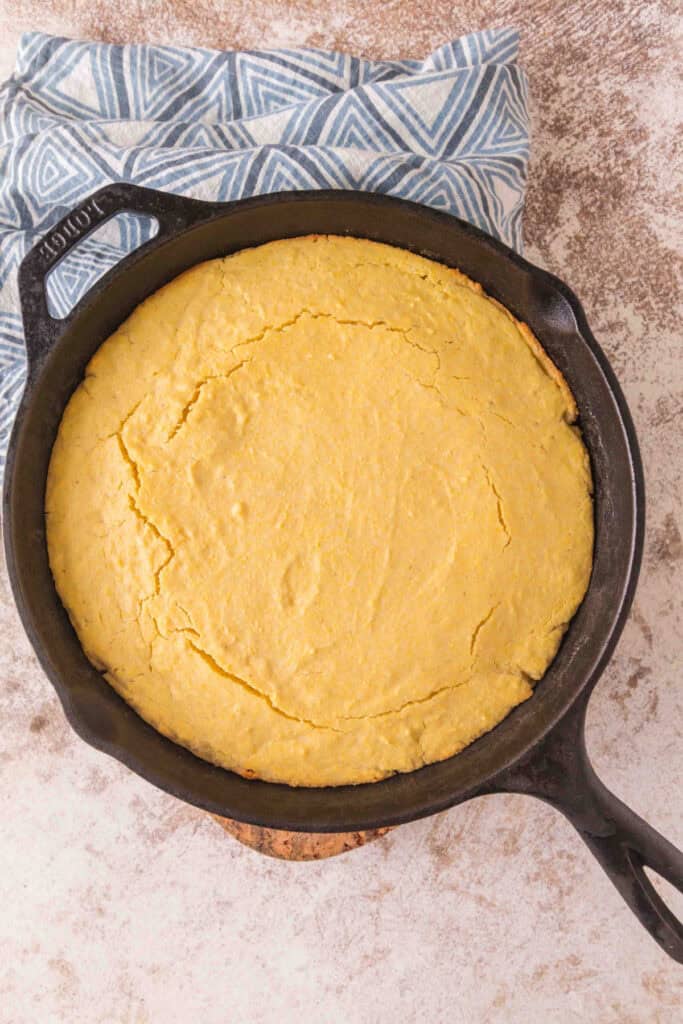 Freshly baked golden sourdough discard cornbread in a cast iron skillet, cooling on a cloth.