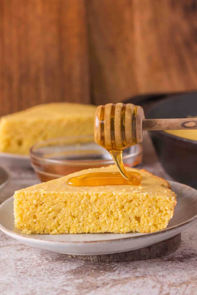 Close-up of cornbread slice with honey drizzled on top, showing moist crumb texture.