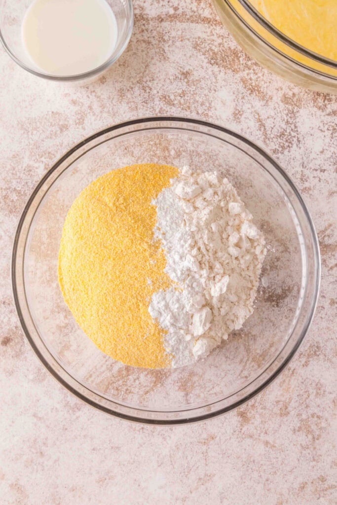 Mixing bowl with yellow cornmeal and flour added together for dry ingredient mixture.