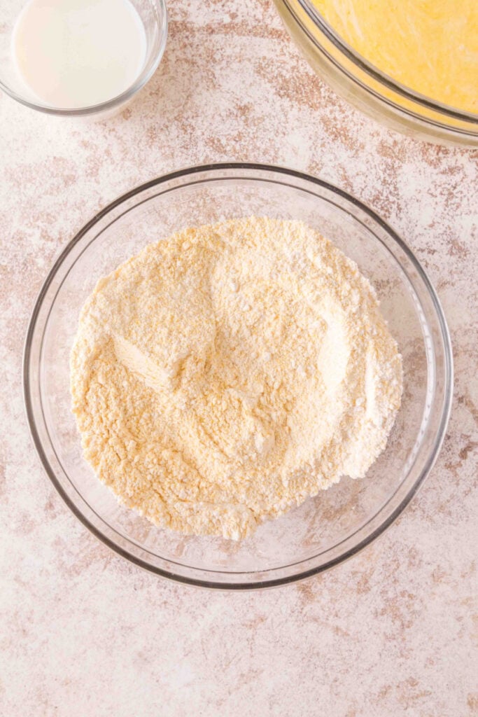 Cornmeal and flour whisked together in a mixing bowl for the dry base of cornbread.