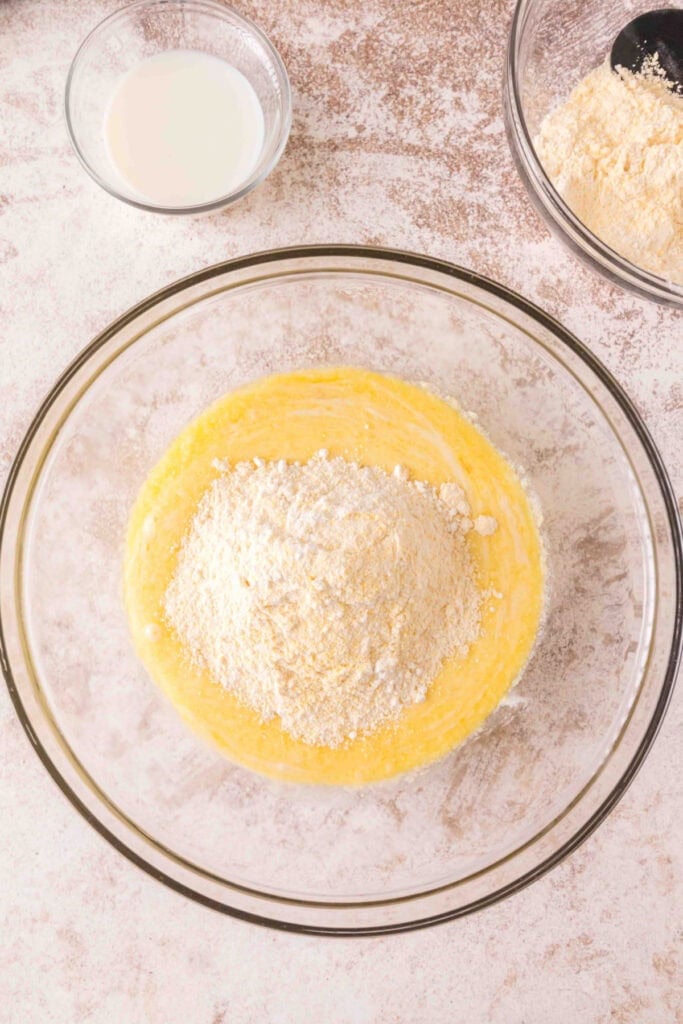 Bowl of wet cornbread batter with dry flour and cornmeal mixture poured on top.