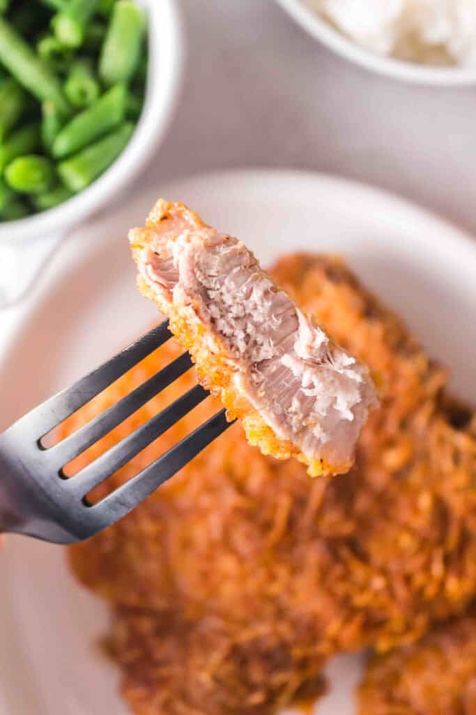 Close-up of a bite of juicy air fryer pork chop on a fork showing tender inside and crispy coating.