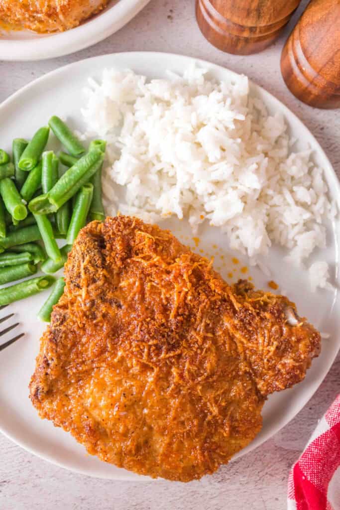 Overhead view of crispy bone-in pork chop plated with green beans and rice, ready to serve.