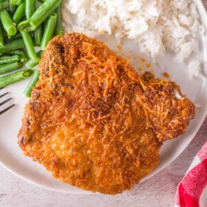 Square image of golden air fryer bone-in pork chop with green beans and rice on a white plate.