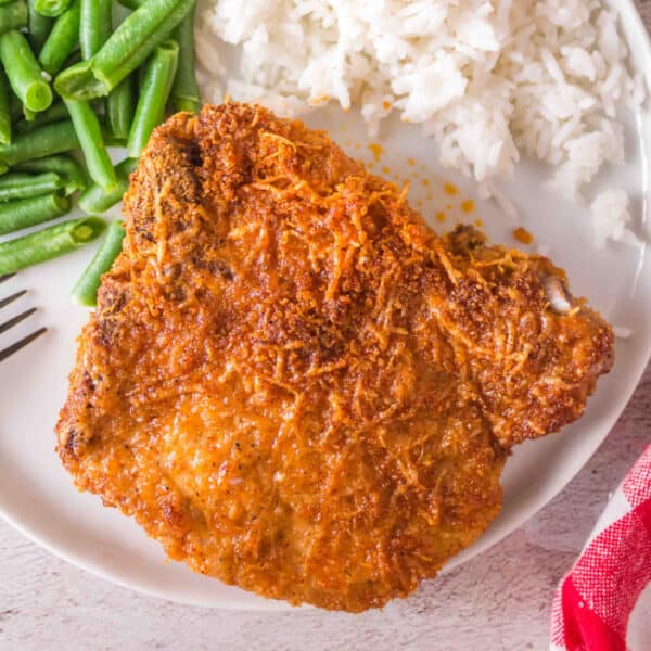 Square image of golden air fryer bone-in pork chop with green beans and rice on a white plate.